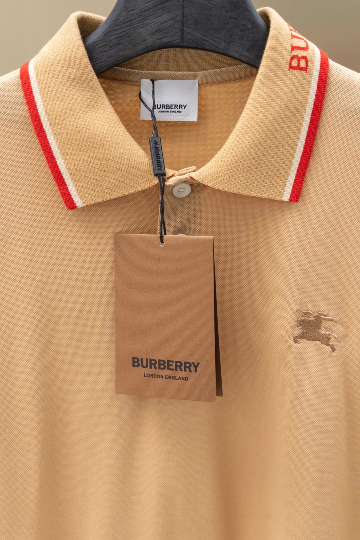 Light beige polo shirt front with button placket, red-trim collar, hanging tag