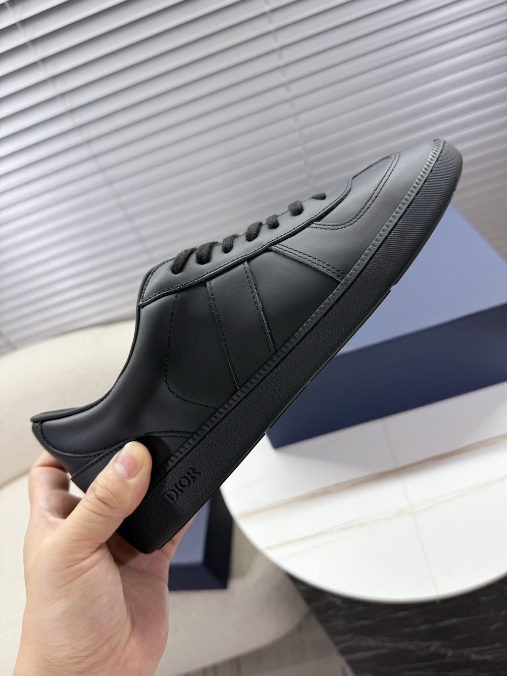 Dior black leather sneaker held by hand, showing laces and side logo.
