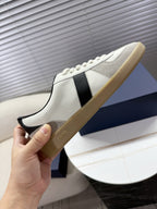 Hand holding white sneakers with black side panel, cream sole, lace-up front