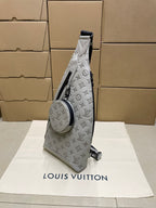 Monogram sling bag with top strap tab and circular logo patch on white-gray body