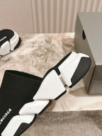 White and black knit slide sandals with Balenciaga logos and thick white soles.