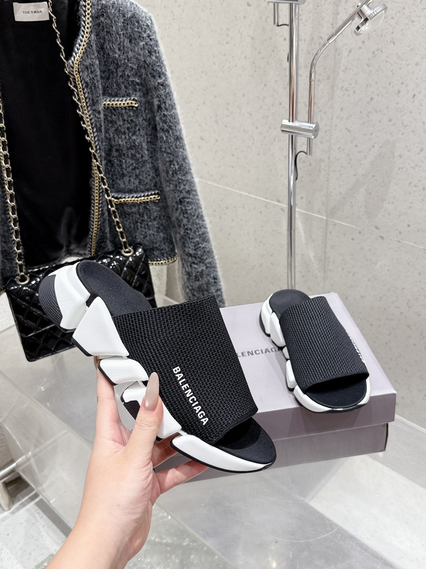 Balenciaga black slide sandals with knit strap and white sole, hand holding pair