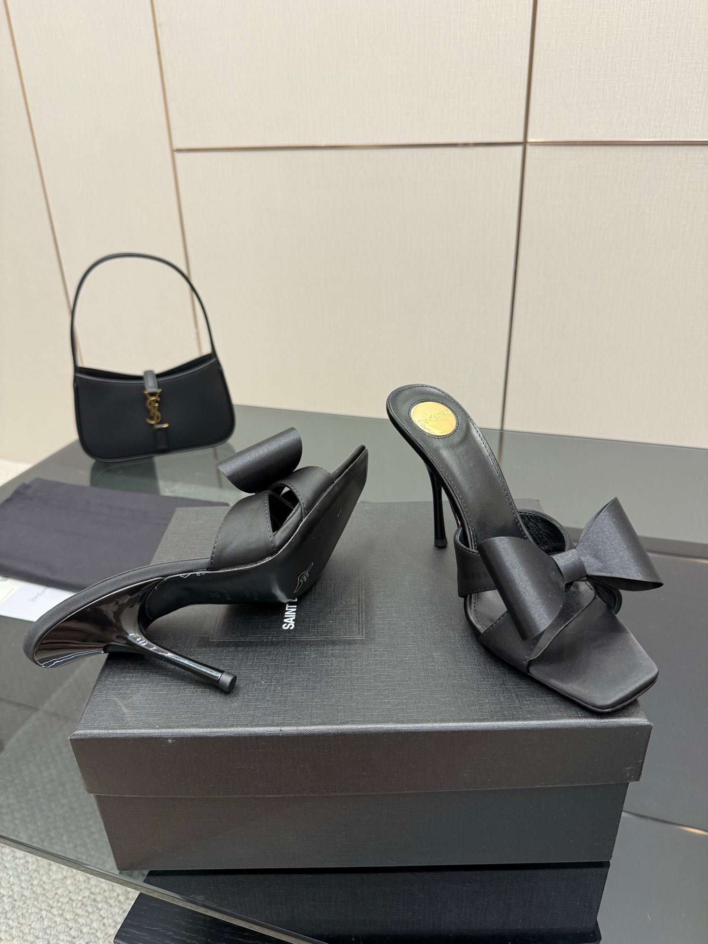 YSL black high-heel mule sandals with wide bow straps, side view on display box