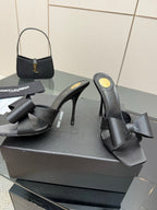 YSL black high-heel mule sandals with wide bow detail, angled view on display