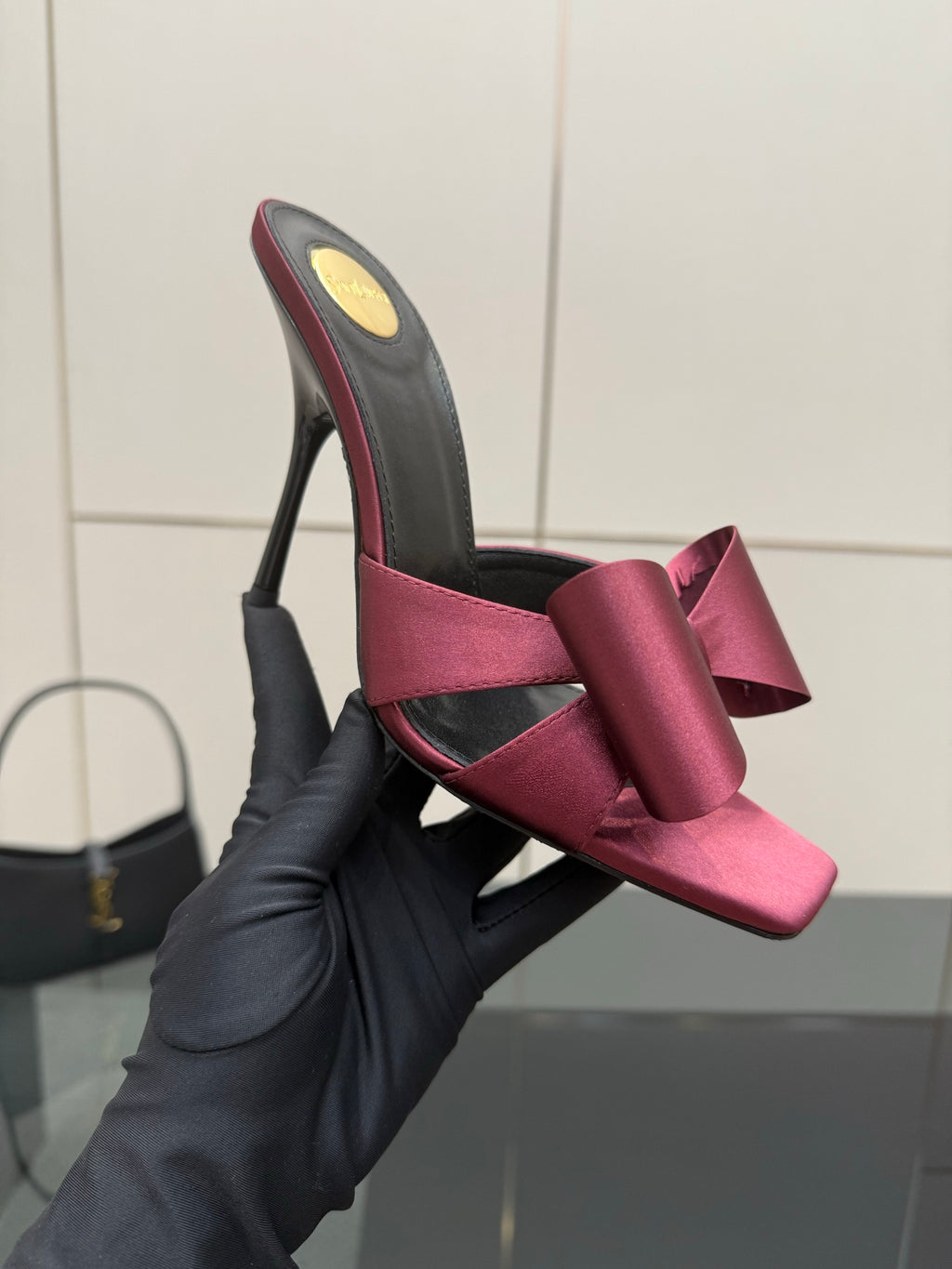 YSL pink satin bow mule with black upper, held by a black-gloved hand