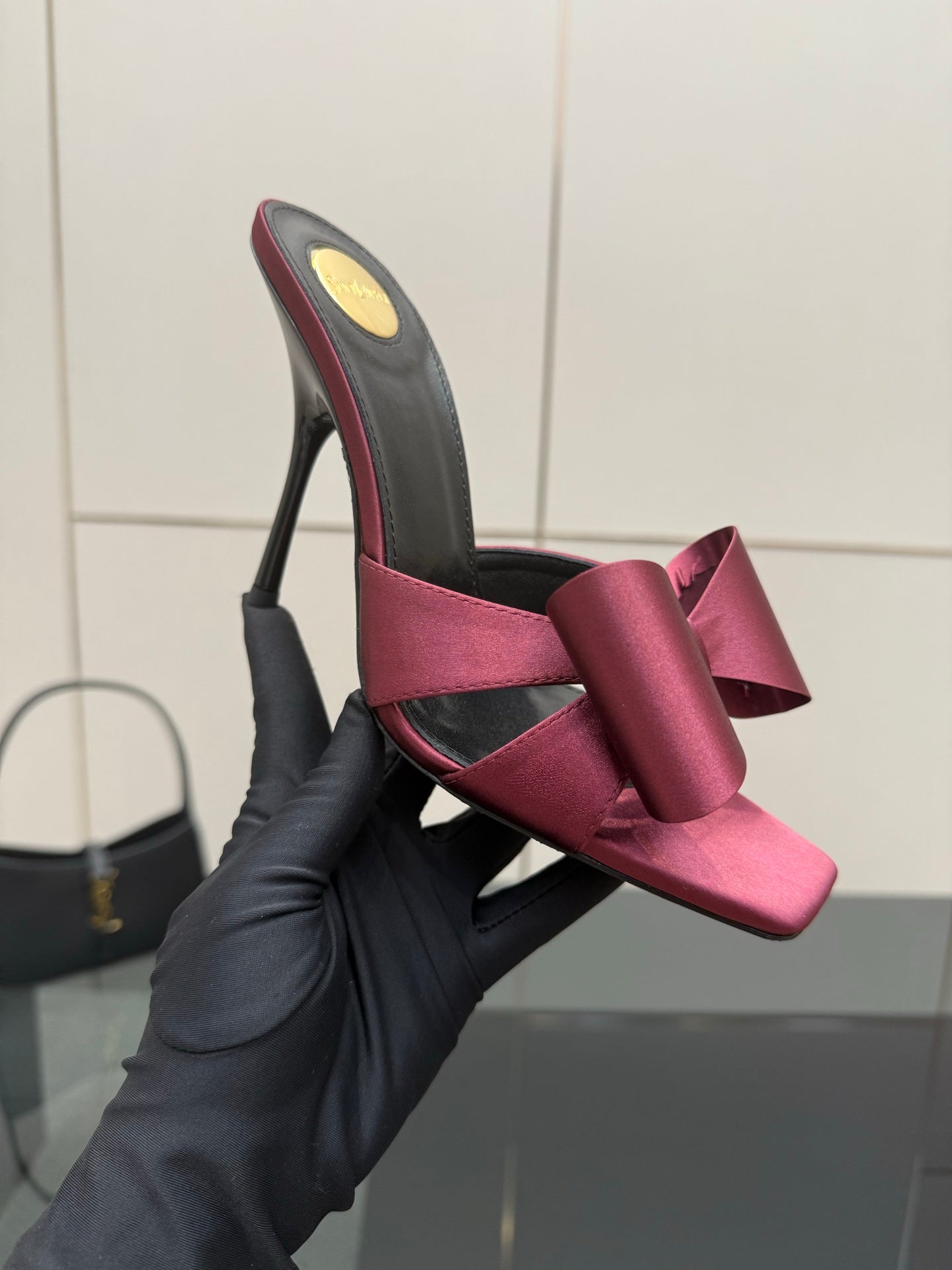 YSL pink satin bow mule with black upper, held by a black-gloved hand