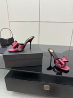 YSL pink satin bow mules with black high heel, angled on display box