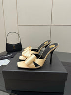 Beige heeled mules with black strap and gold-tone bow detail, stiletto heel