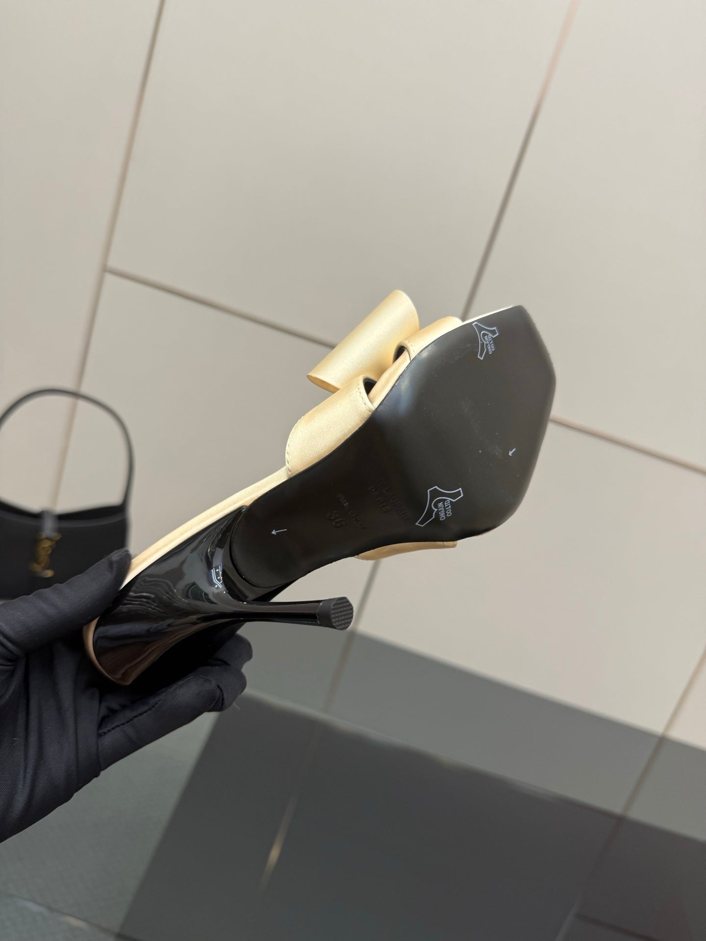 Black patent mule heel with beige bow strap and subtle logo, curved stiletto