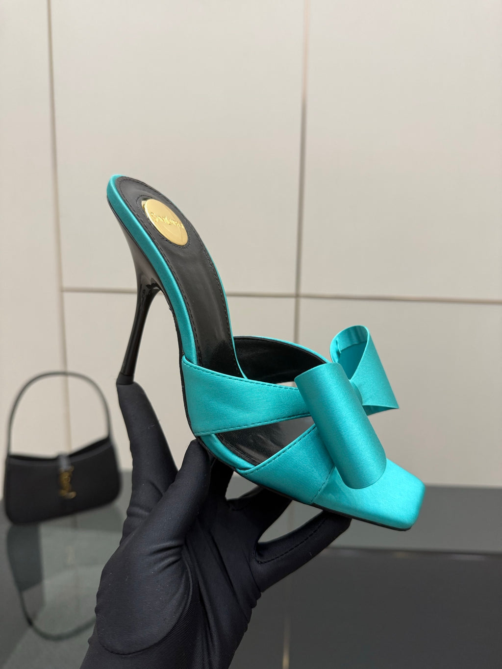 Turquoise bow mule heel held in glove, slender stiletto, black interior