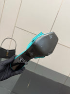 Turquoise mule heel underside held in hand, black sole with small logo emblems
