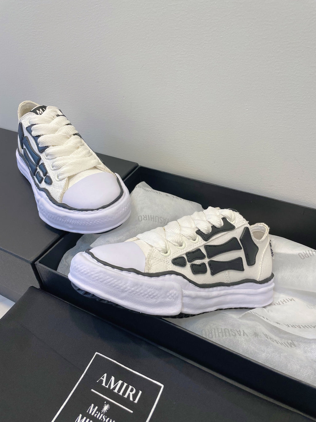 Amiri white and black lace-up sneakers, one shoe reclined on box