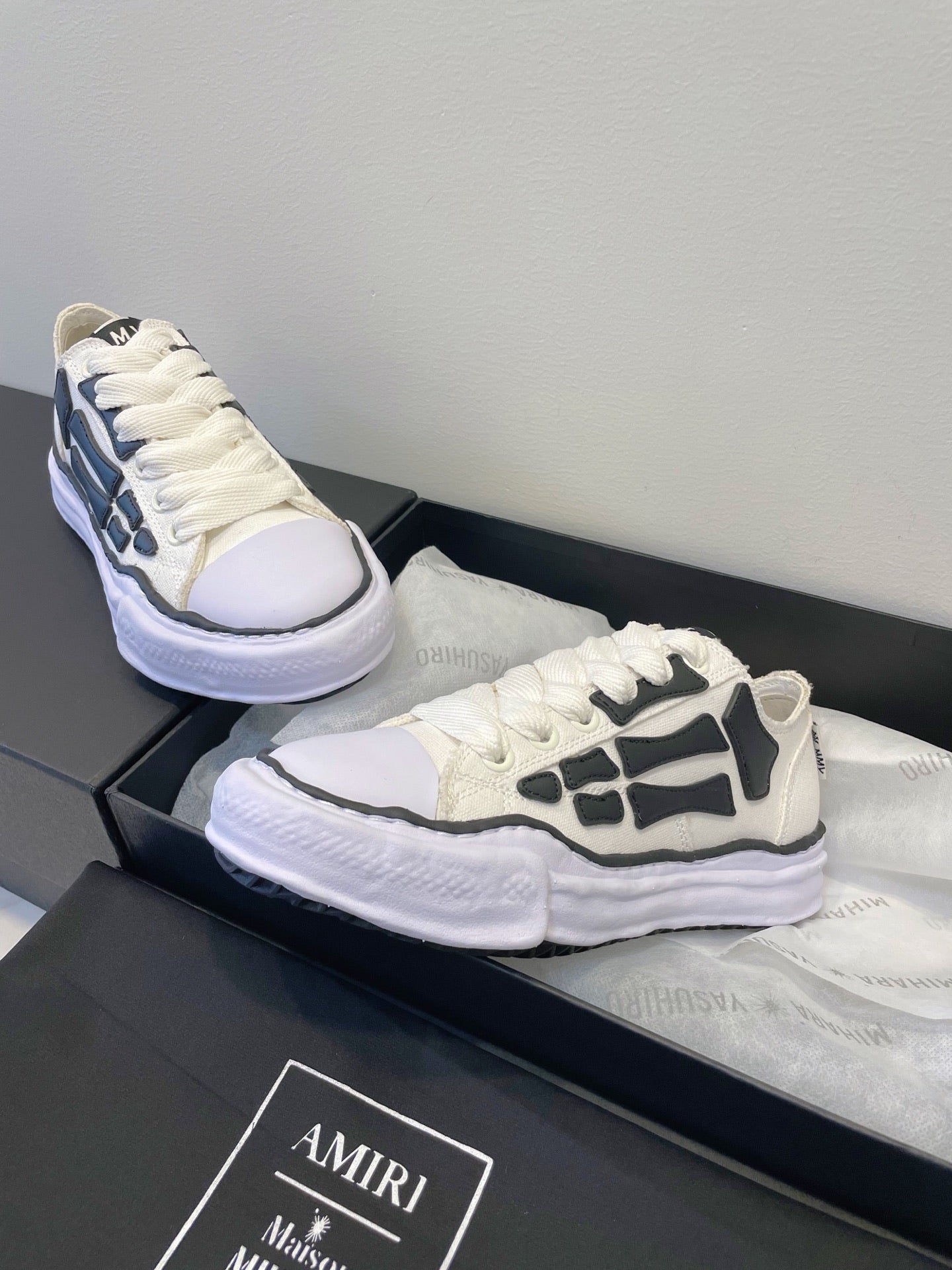 Amiri white and black lace-up sneakers, one shoe reclined on box