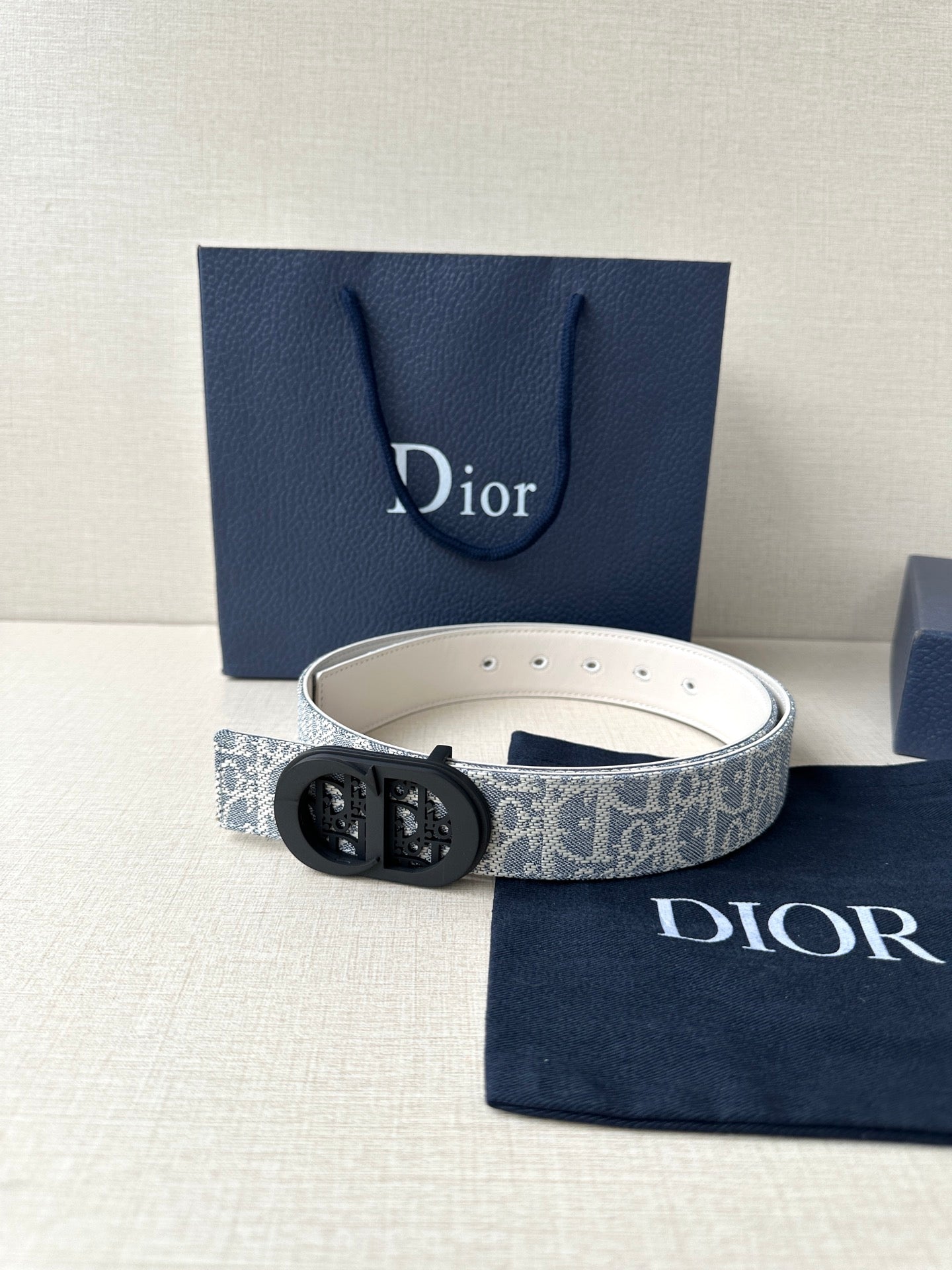 Dior belt with light patterned strap and black oval logo buckle