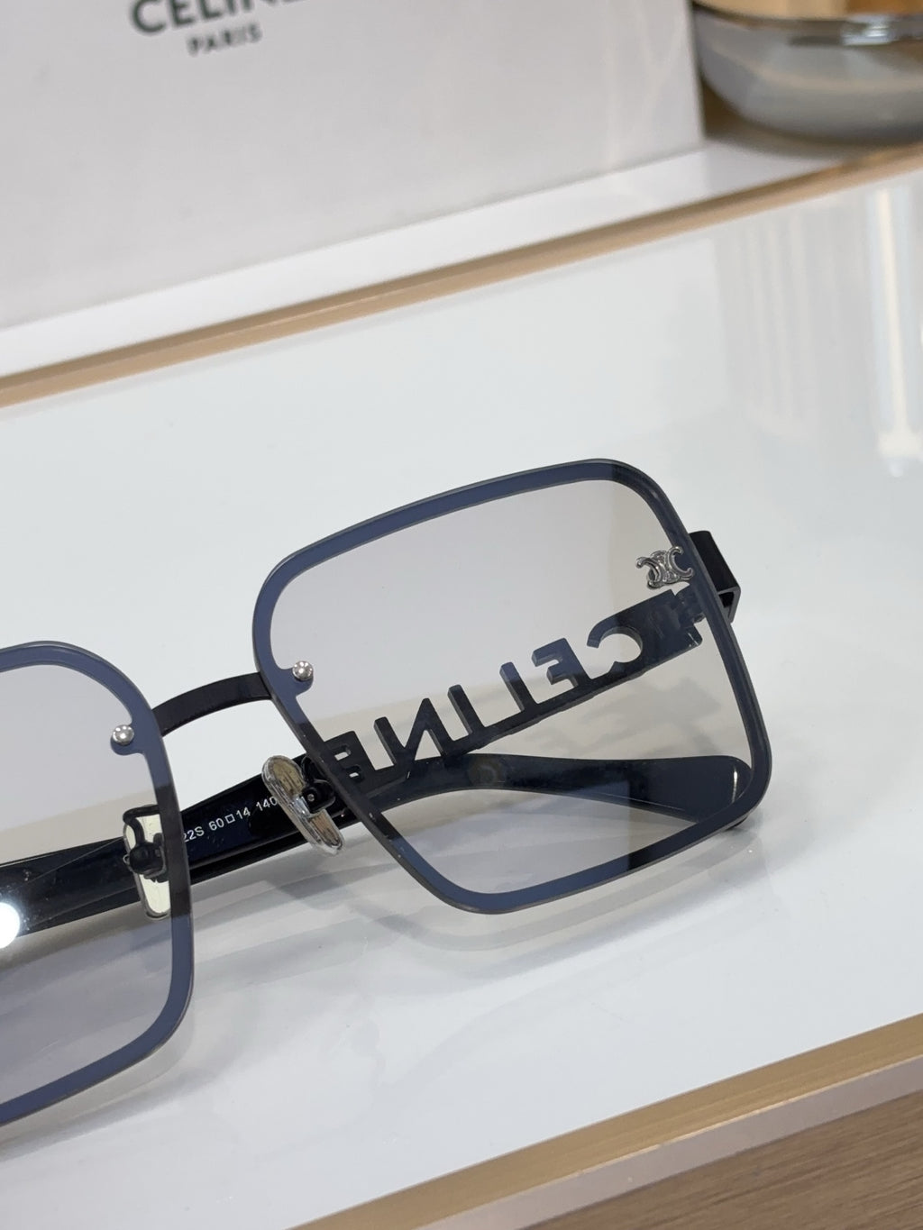 Sunglasses temple close-up with dark frame, gold logo detail, clear lenses