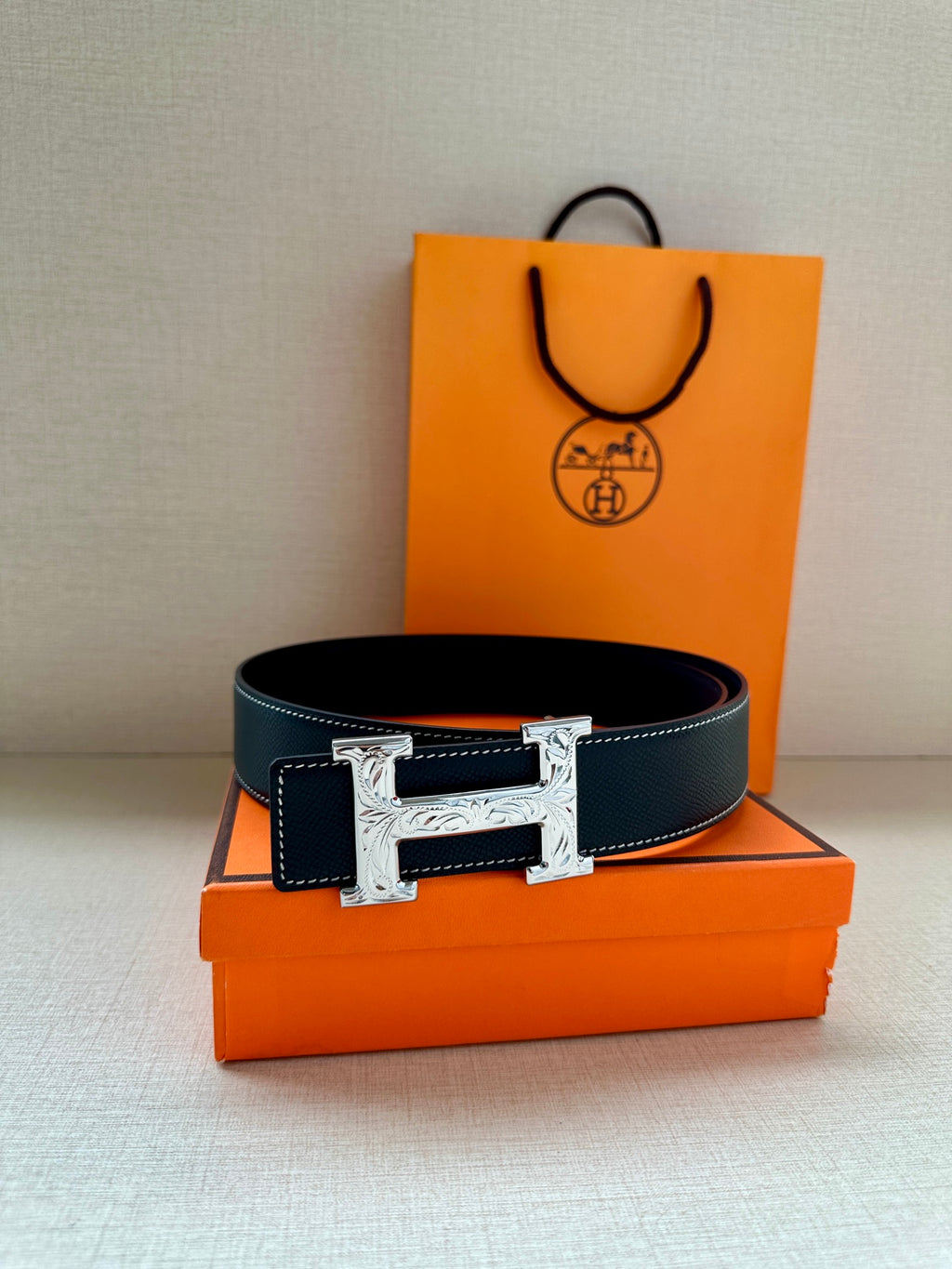 Hermes leather belt in dark blue with silver buckle, on orange box