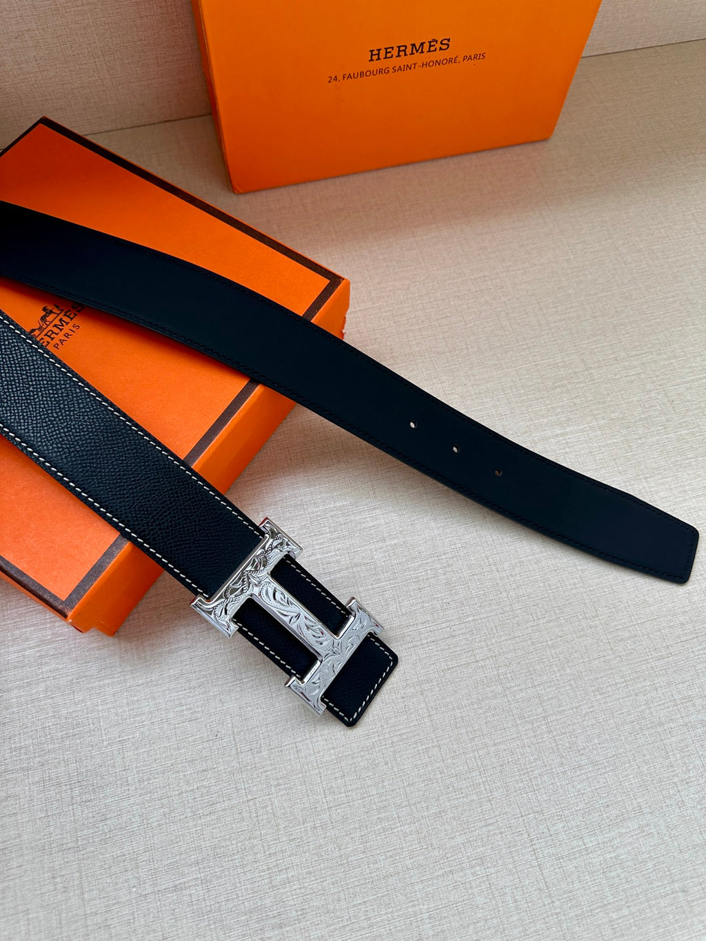 Dark leather belt with silver-tone H buckle, laid flat beside gift boxes