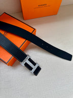 Dark leather belt with silver-tone H buckle, laid flat beside gift boxes