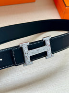 Dark leather belt close-up with embossed stitching and silver-tone H buckle