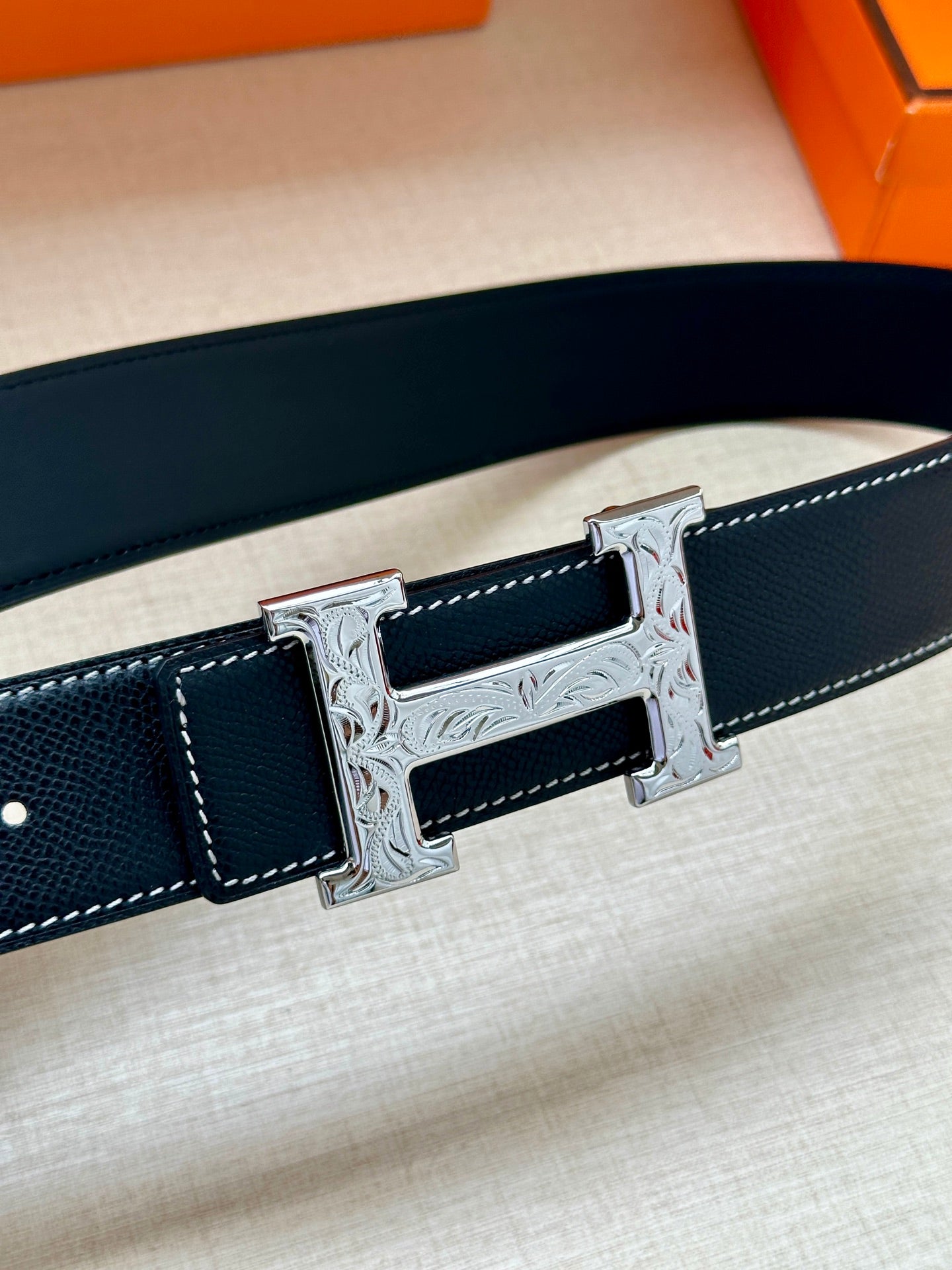 Dark leather belt close-up with embossed stitching and silver-tone H buckle