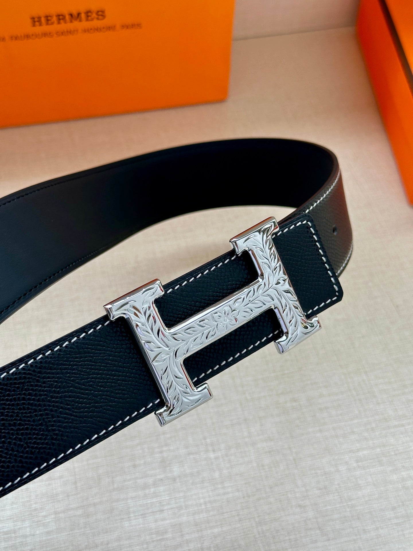 Close-up of Hermes dark leather belt with embossed silver-toned H buckle