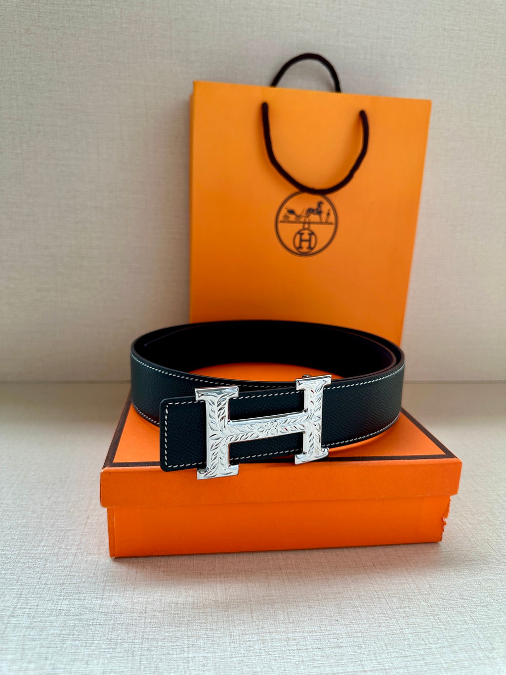 Hermes dark leather belt with silver-toned H buckle, placed on box