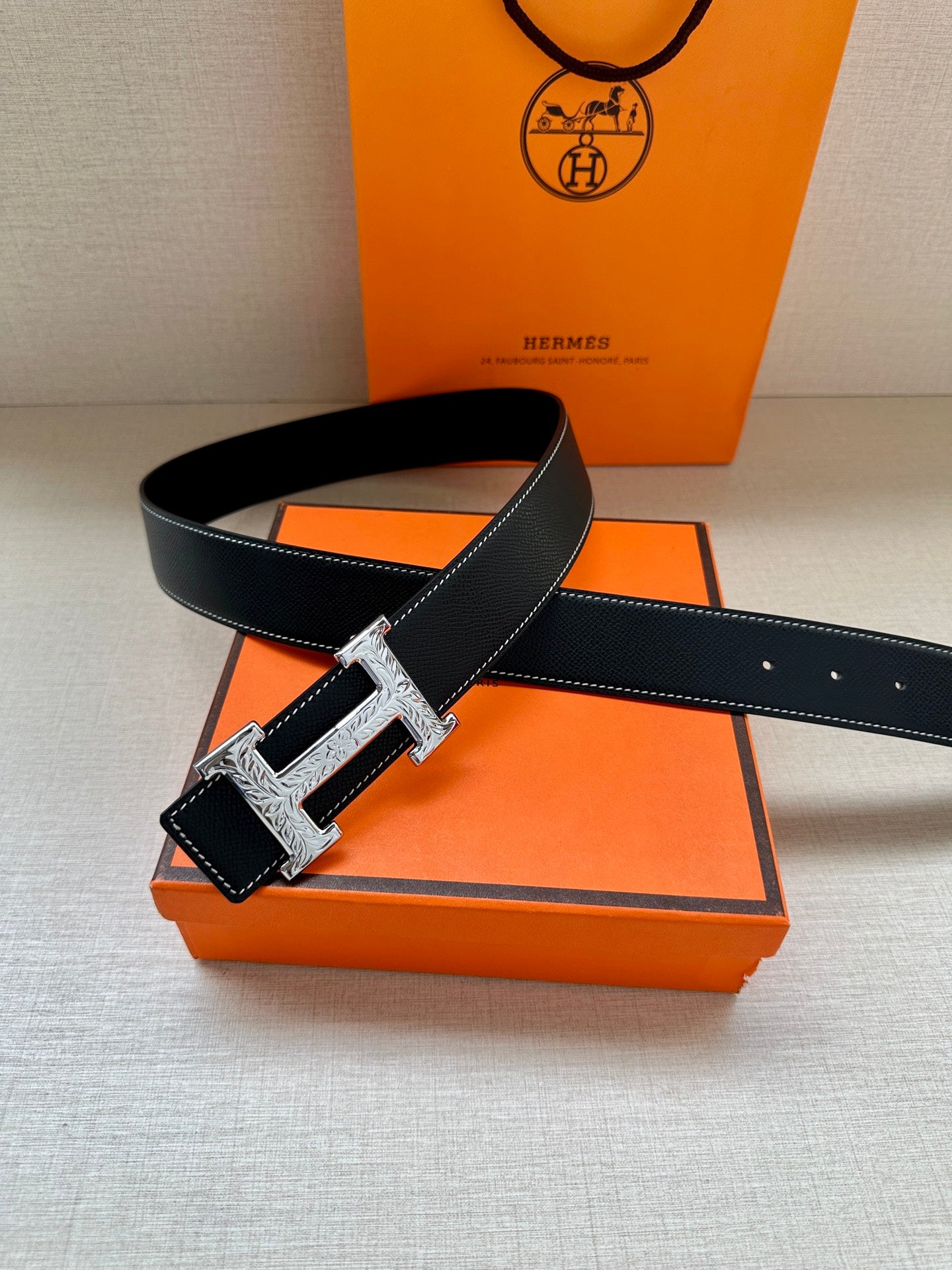 Hermes dark leather belt with silver-toned H buckle, angled view