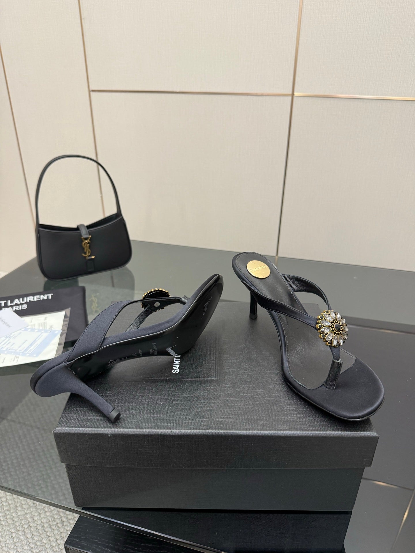 Women’s black high-heel sandals with thin straps and gold-toned jeweled ornament on the toe.
