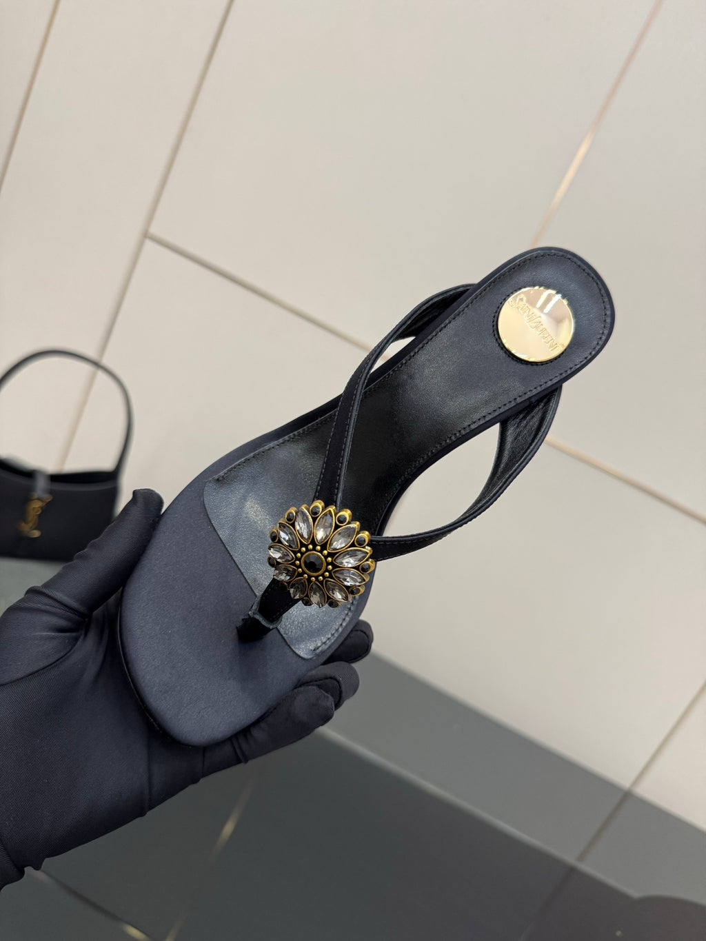Women’s black high-heel sandal in hand with gold-toned floral jeweled toe embellishment.
