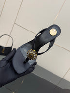 Women’s black high-heel sandal in hand with gold-toned floral jeweled toe embellishment.