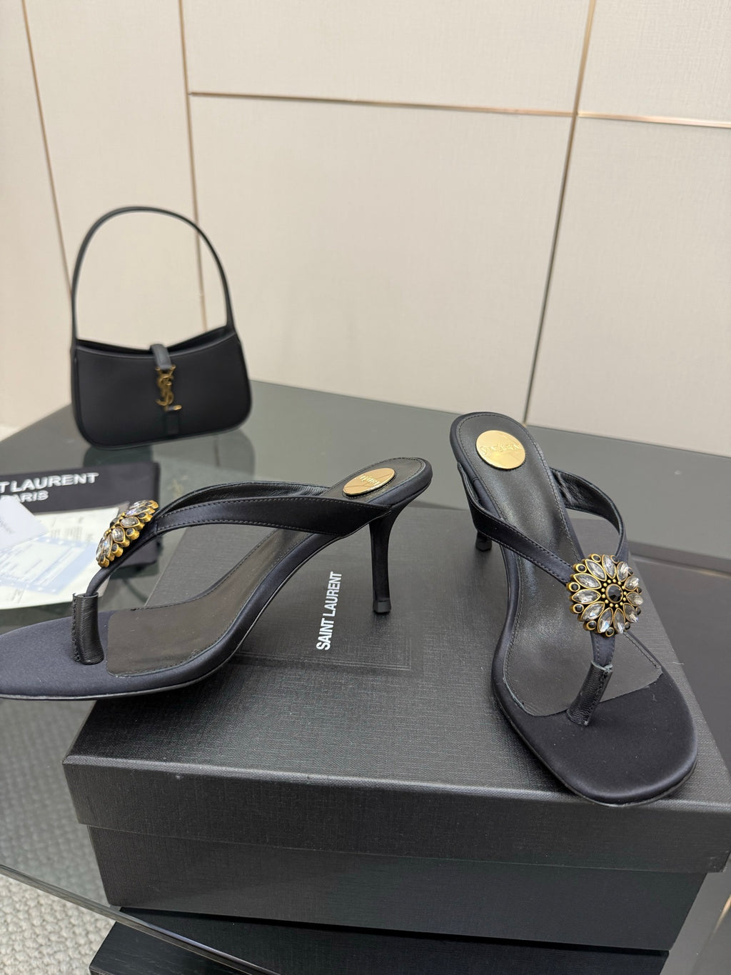 Women’s black high-heel thong sandals with gold-toned jeweled ornament and slim heel.