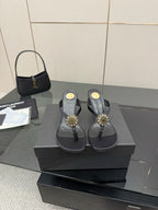 Women’s black high-heel thong sandals on a box with gold-toned jeweled toe embellishments.