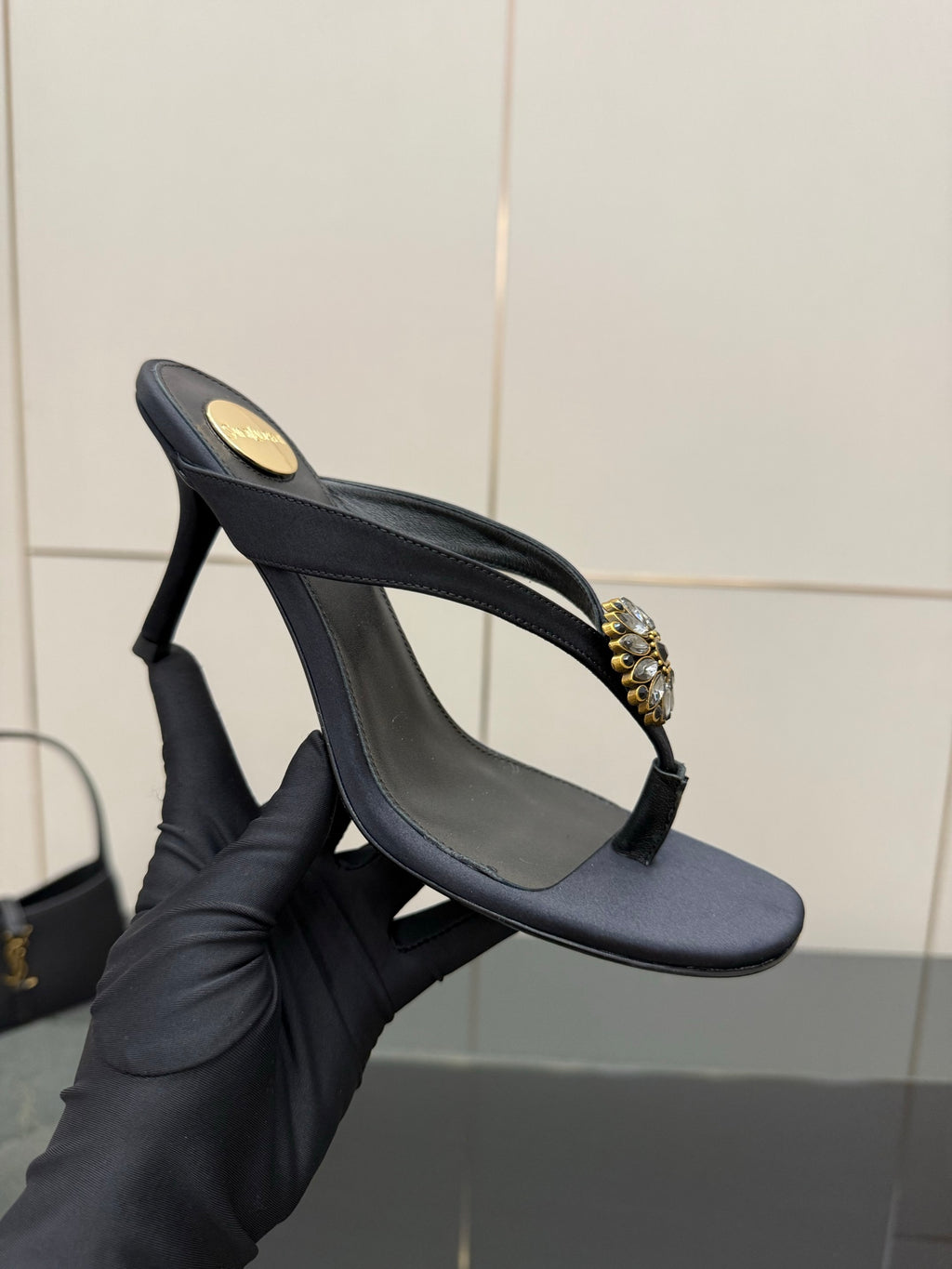 Women’s black slingback high-heel sandal held in a hand, with gold-toned jeweled toe ornament.