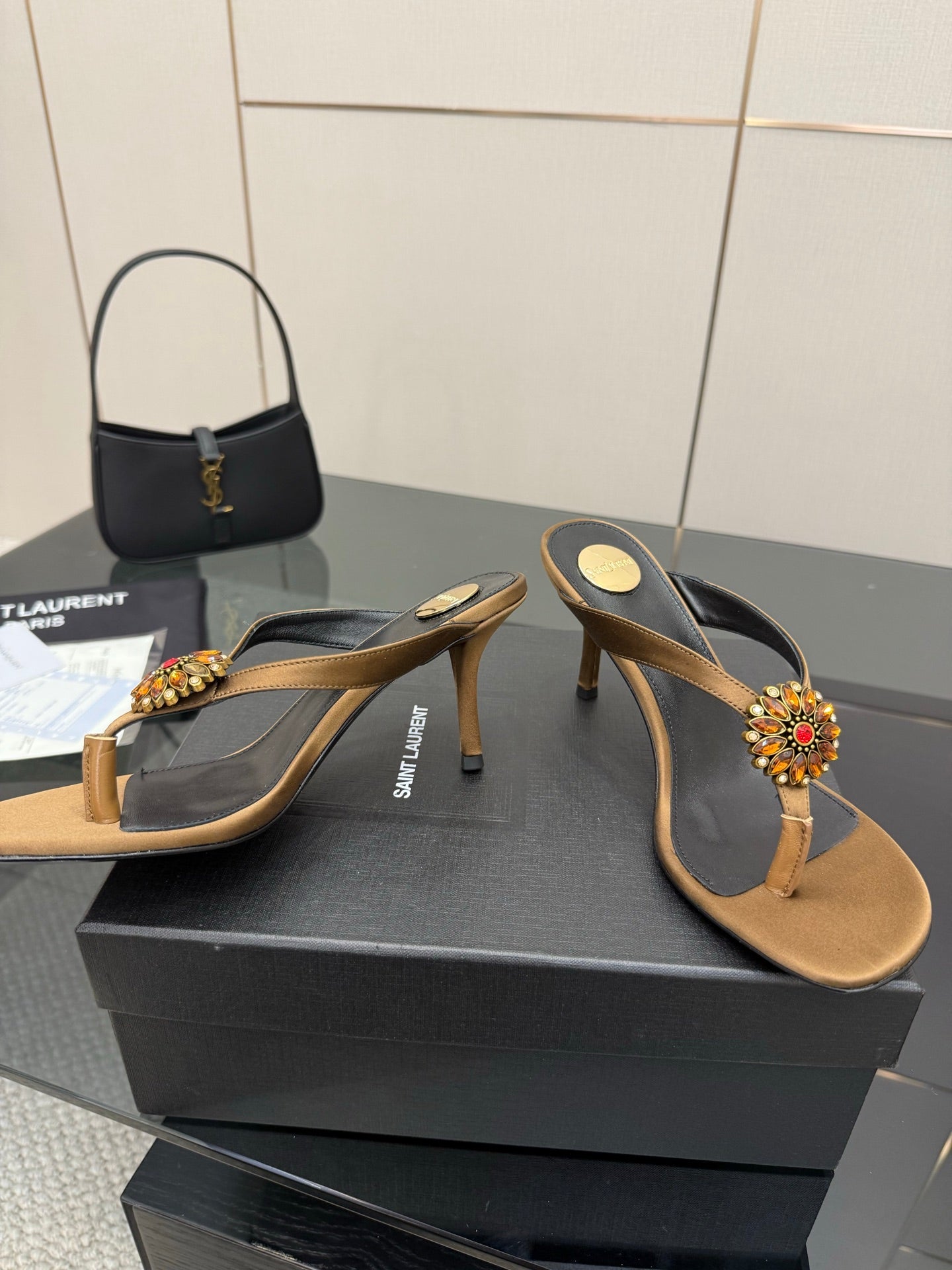 Two YSL thong heeled sandals with tan footbed, black straps, and jeweled flower