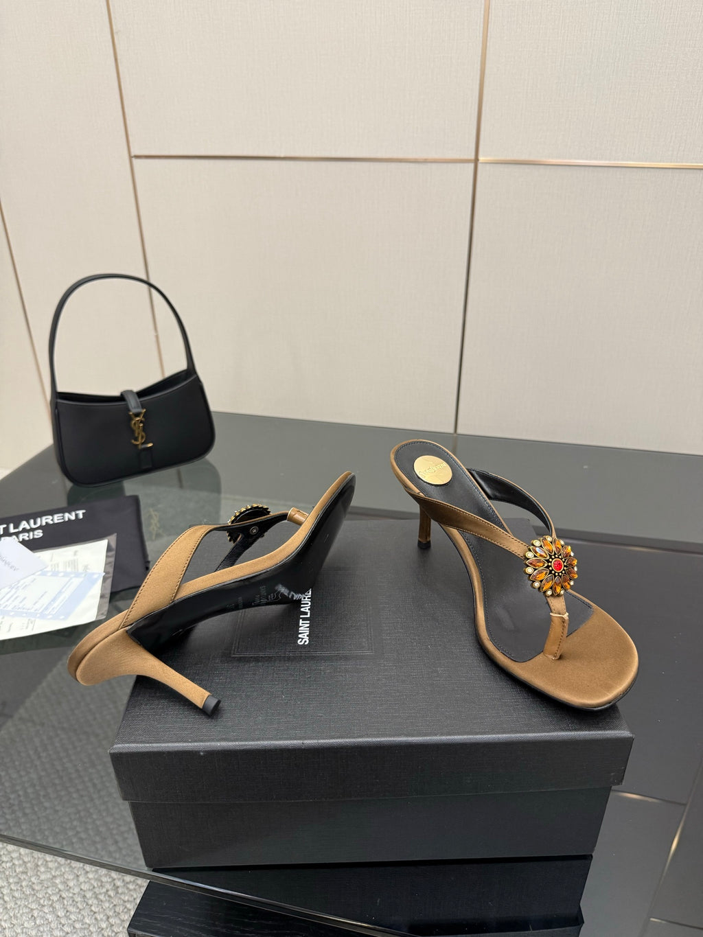 Side view of thong heeled sandals with tan footbed, black straps, jeweled flower