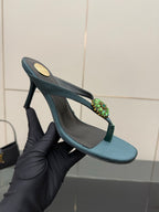 Women's teal heeled sandal held in hand, jeweled floral strap detail