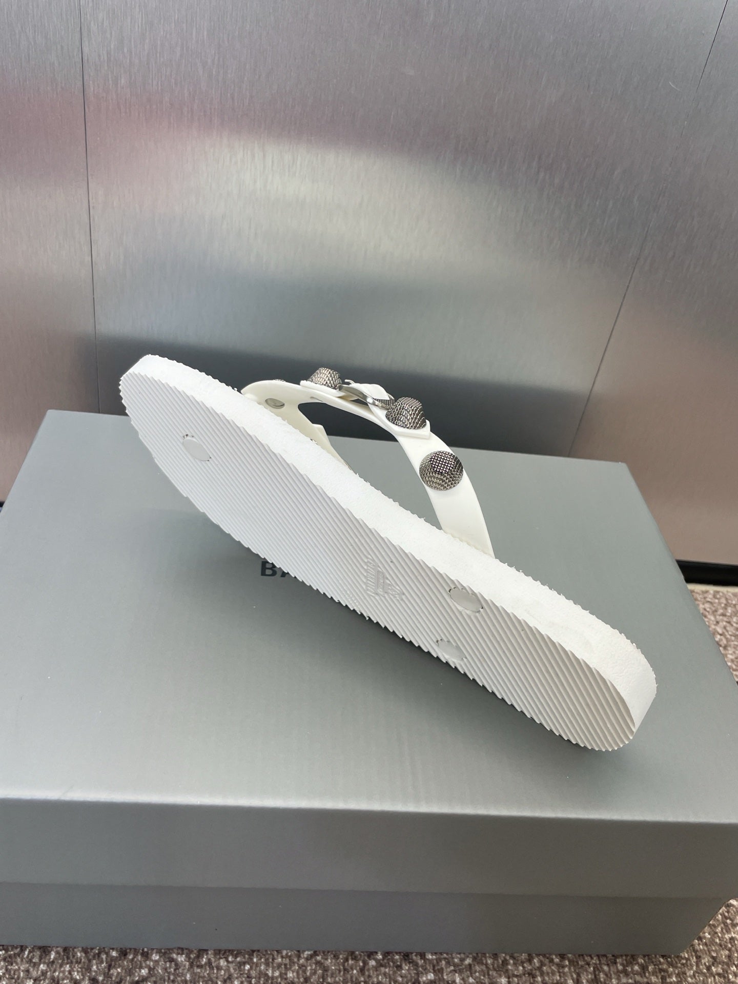 White thong sandal with studded straps and silver-tone hardware, angled