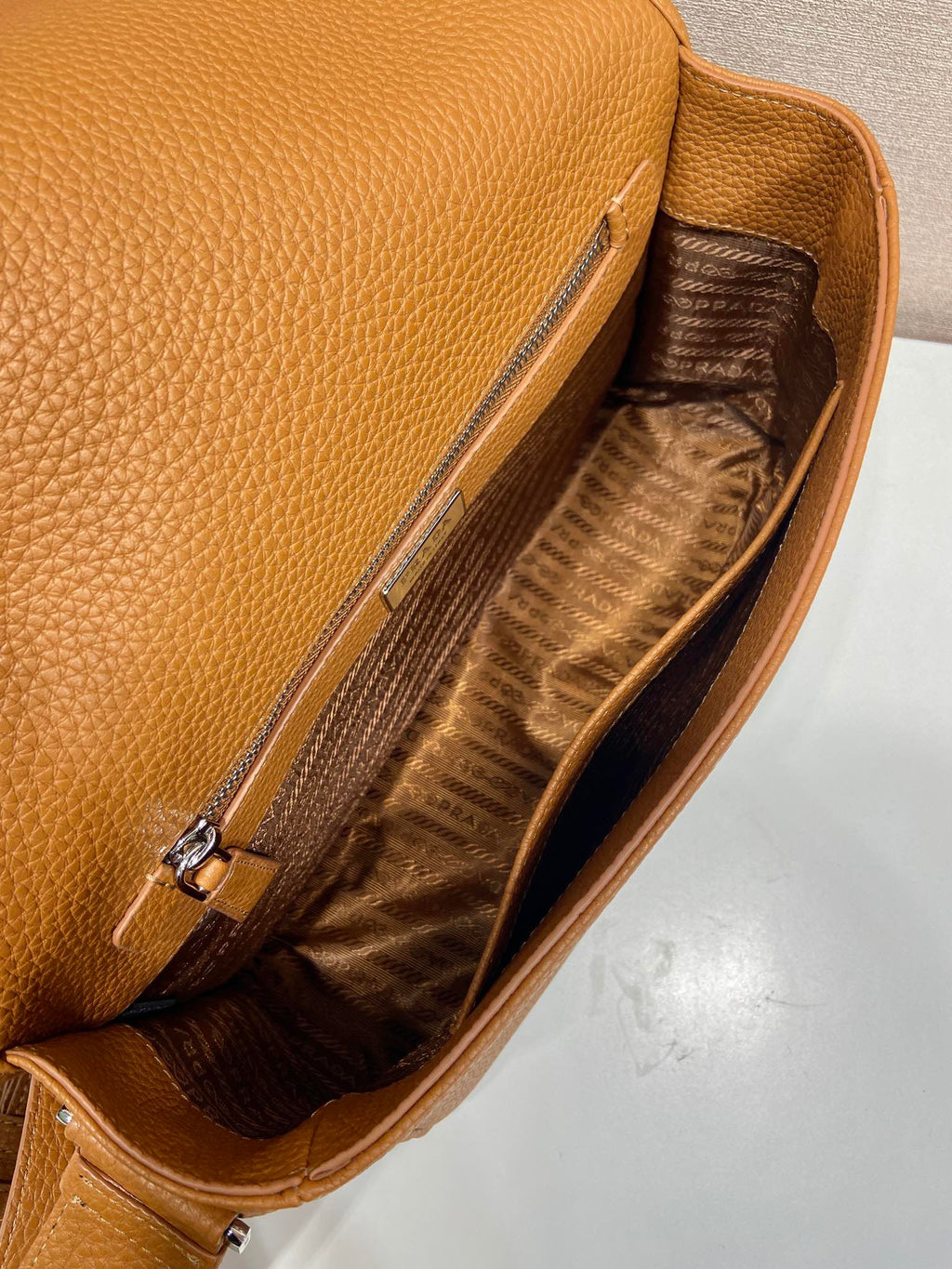 Prada leather crossbody bag interior with open top and zipper pocket, fabric lining