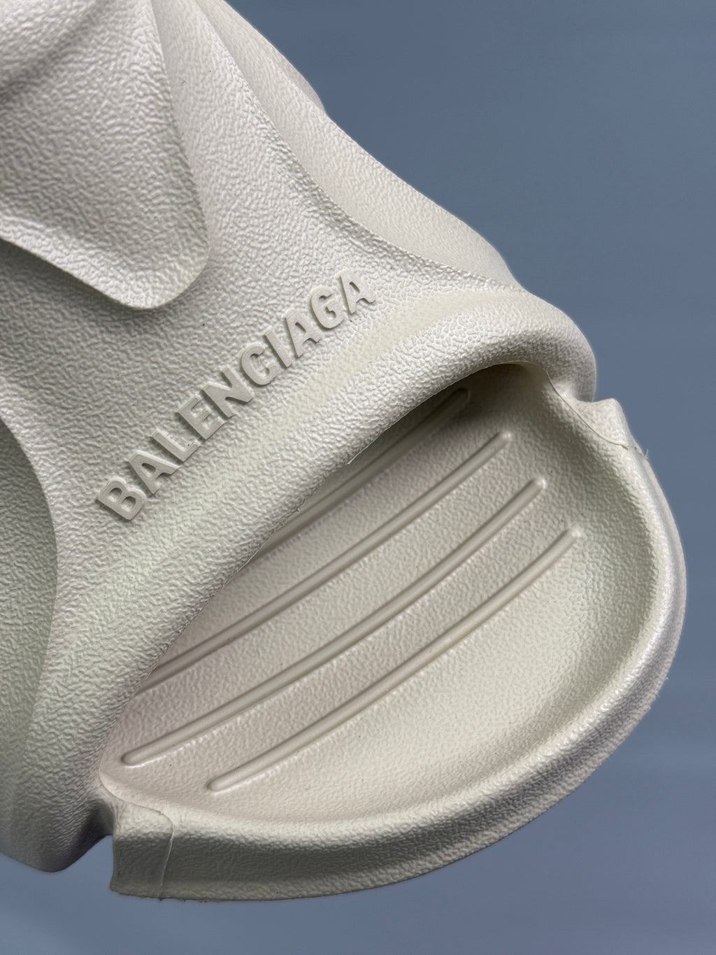 Cream slide sandal side close-up with embossed BALENCIAGA text and ribbed traction tread