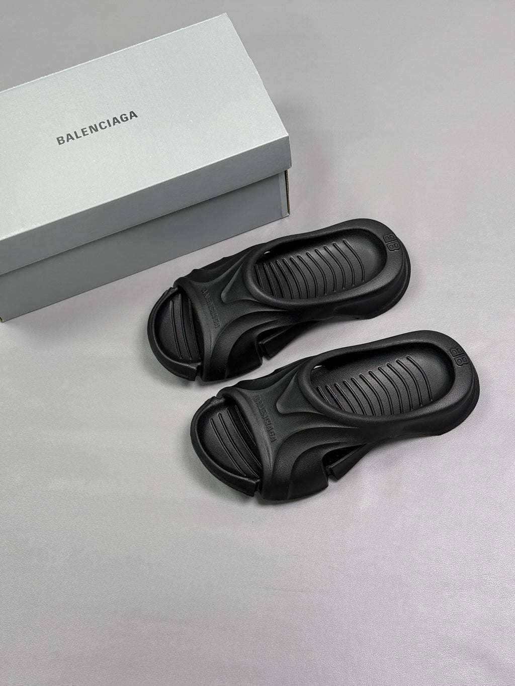 Two black Balenciaga slide sandals with the logo box nearby