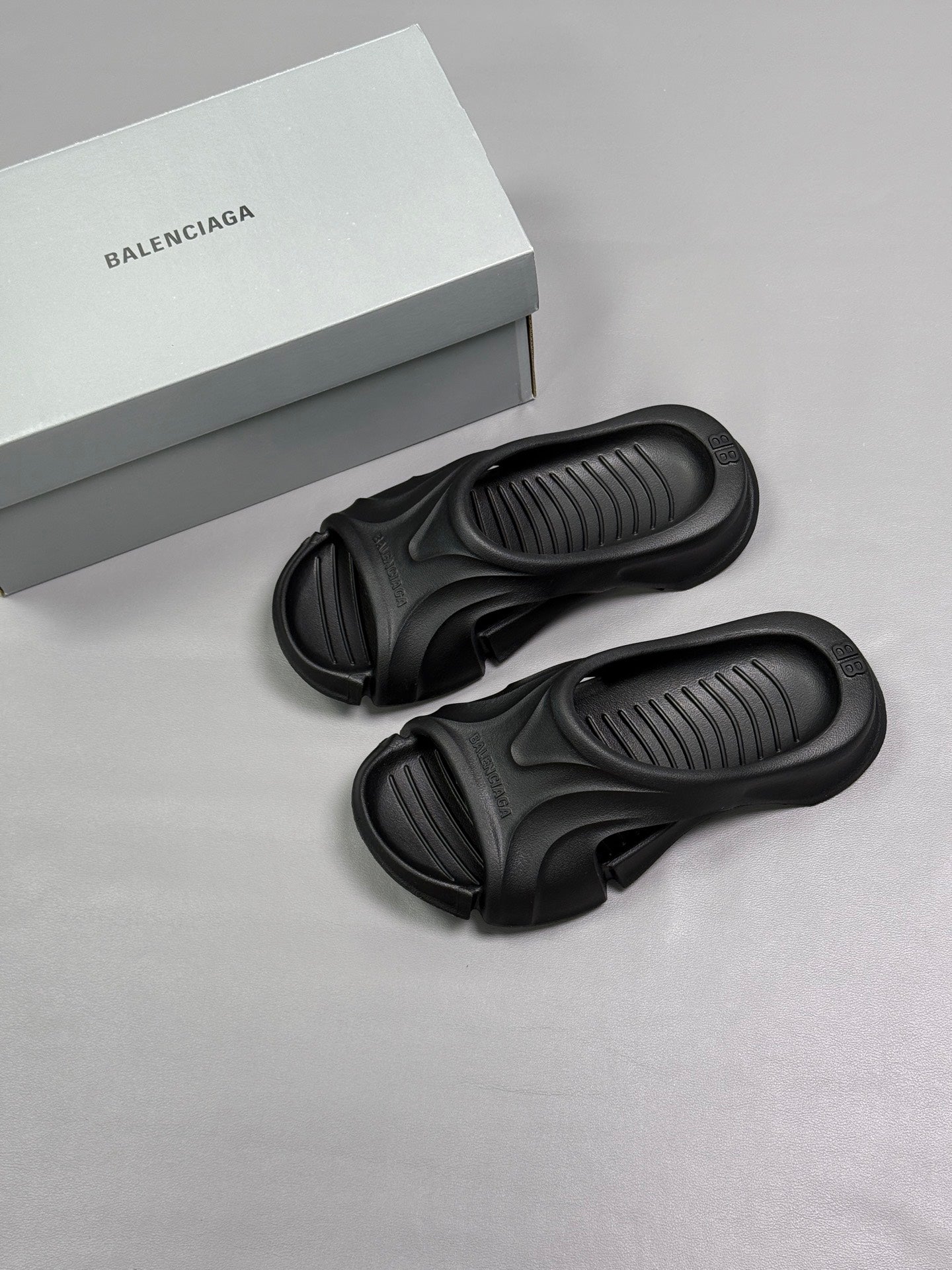 Two black Balenciaga slide sandals with the logo box nearby