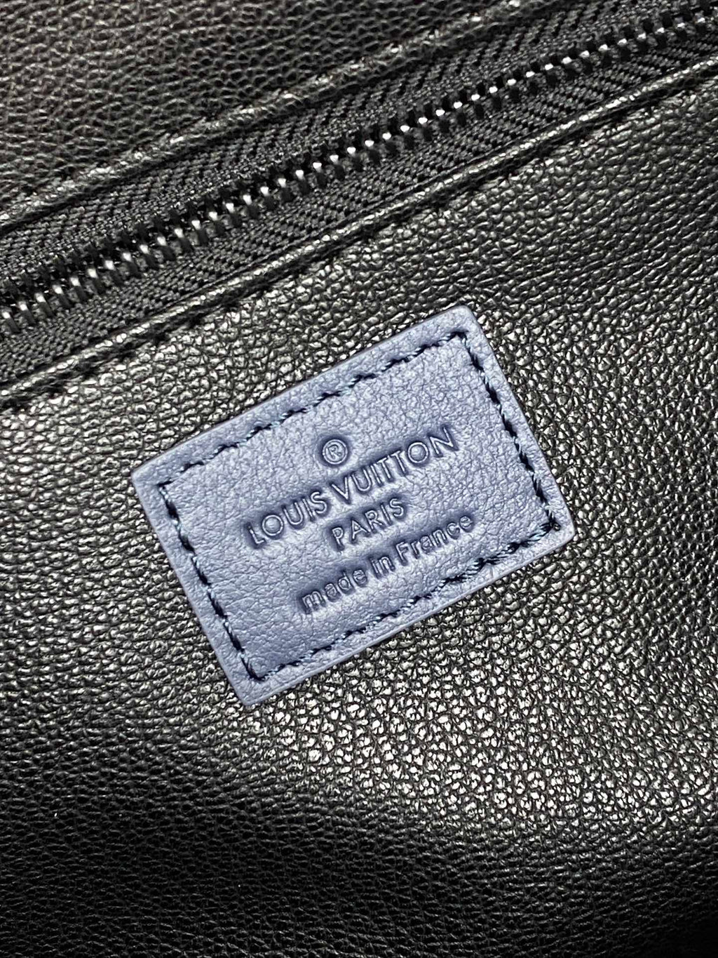 Louis Vuitton bag leather tag patch with Louis Vuitton and Paris imprint on dark blue surface