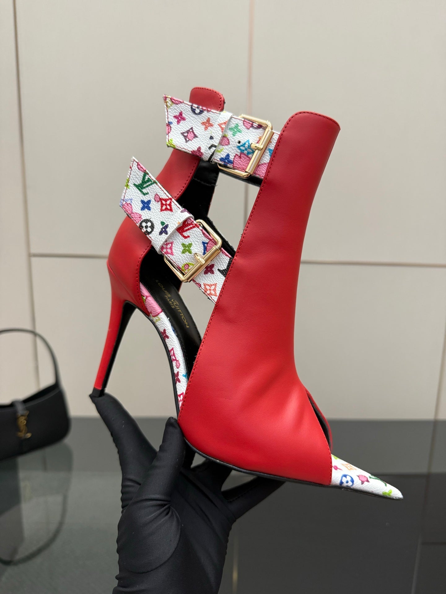 Red ankle boot with multicolor logo-pattern strap and gold buckle detail; stiletto heel