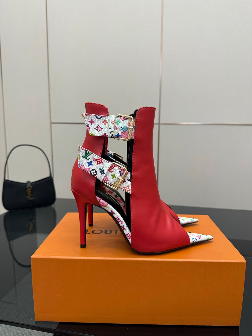 Red ankle boots with multicolor monogram-pattern strap and gold hardware; slender stiletto heel