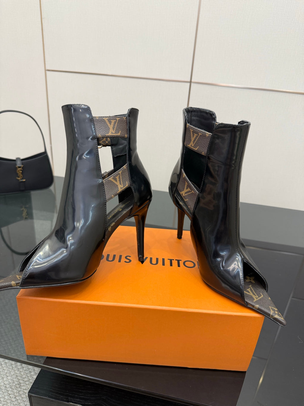 Black patent ankle boots with high stiletto heels and monogram buckle straps.