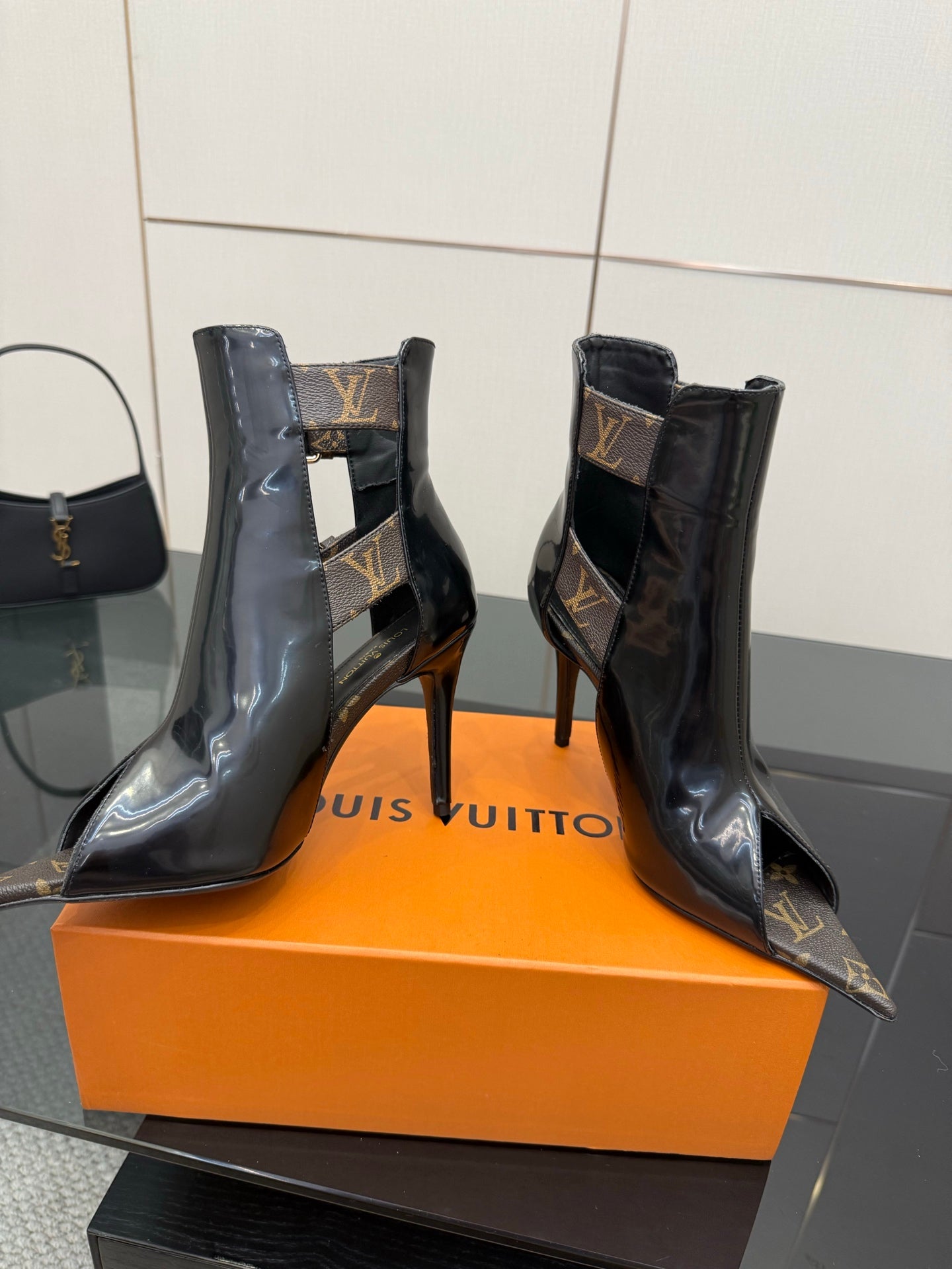 Black patent ankle boots with high stiletto heels and monogram buckle straps.