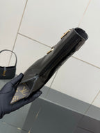 Black patent ankle boot held in hand, side profile with gold hardware.