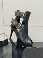 Black patent ankle boot held up, stiletto heel and gold buckle straps.