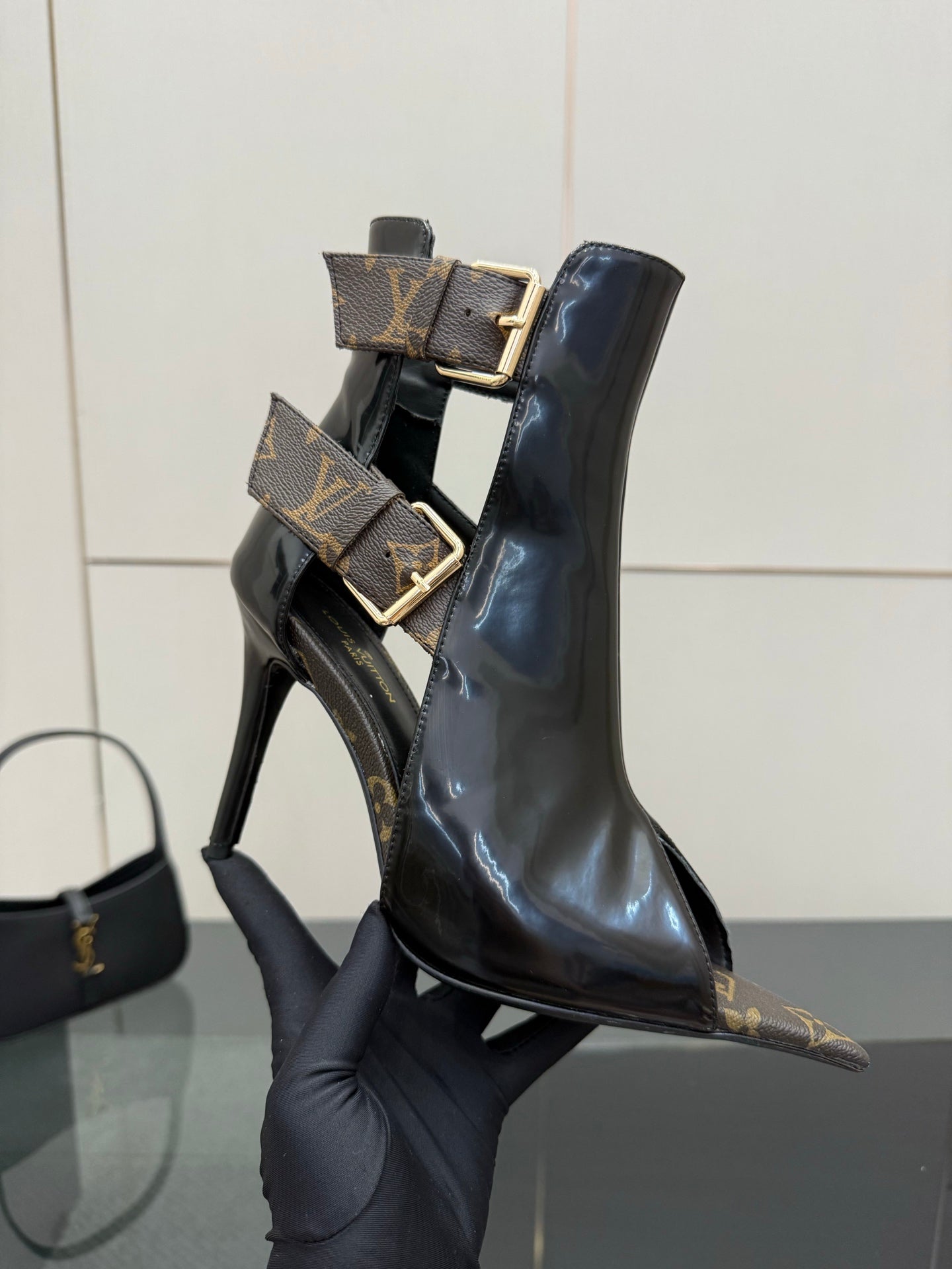 Black patent ankle boot held up, stiletto heel and gold buckle straps.