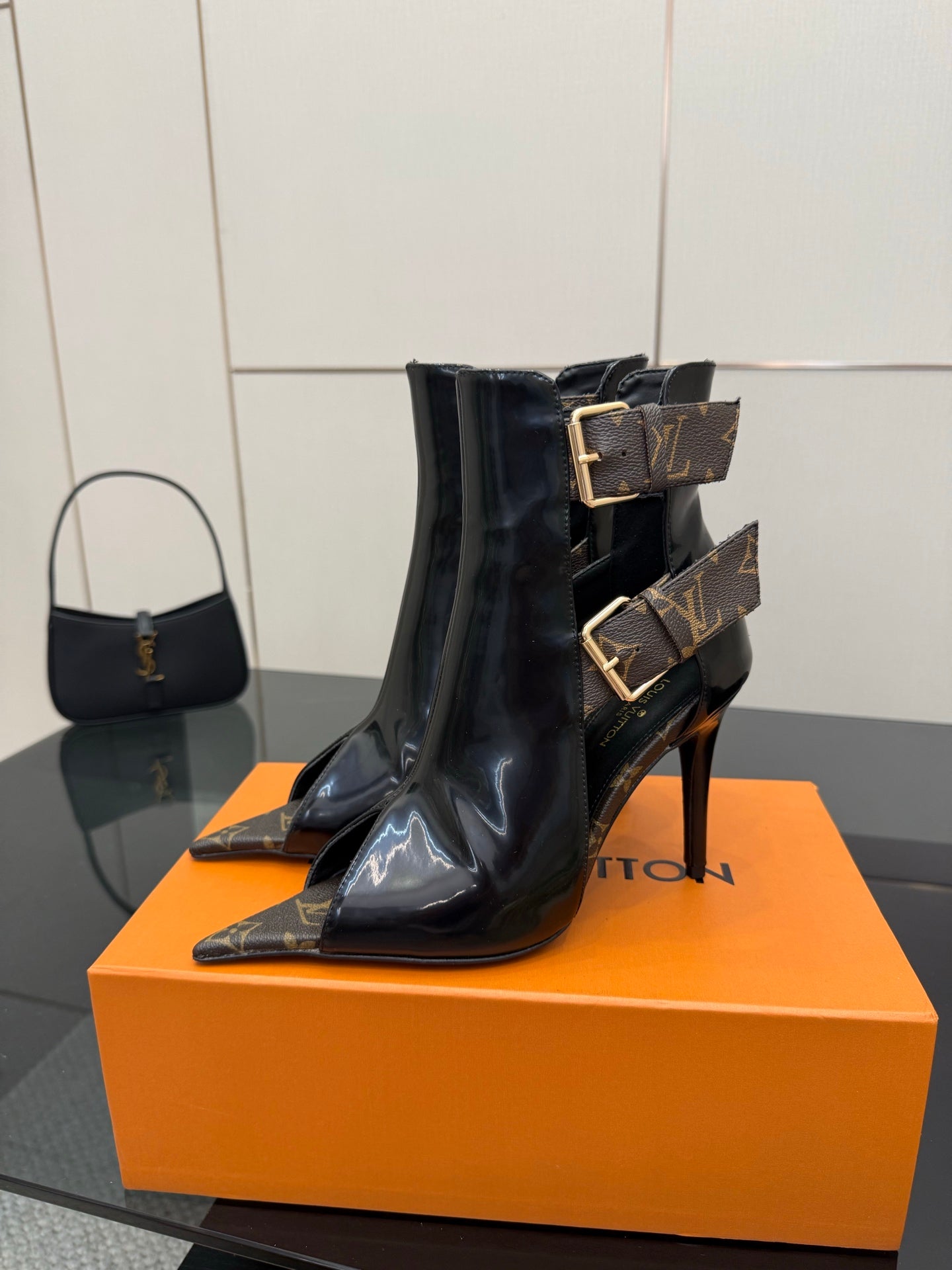 Single black patent ankle boot with gold buckle strap and pointed toe.